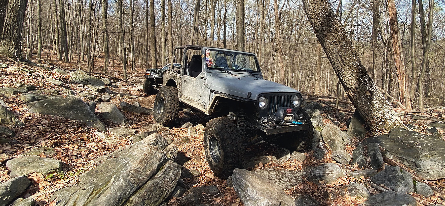 Two lifted Jeeps working up a rock trail through bare hardwoods
